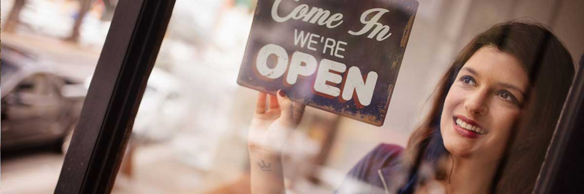 person putting open sign in window of store